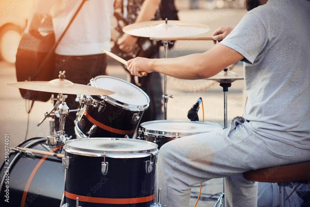 Fototapeta premium A skilled drummer in gray clothes plays a cool drum kit wooden drumsticks at a concert with the band, illuminated by bright lights.