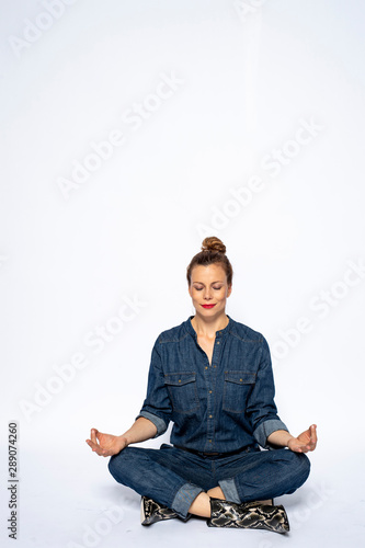 Beautyful woman in Studio in Modern Jeans outfit is sitting in a yoga seat