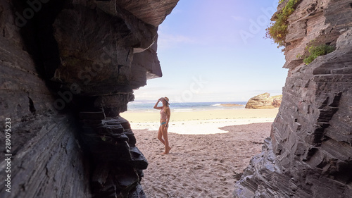 Young woman contemplates a cave made of rocks on a beach in Galicia photo