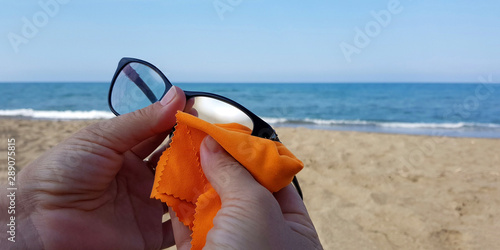 Donna che pulisce occhiali da vista sulla spiaggia photo