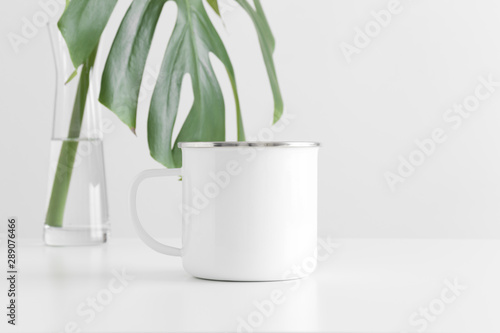 Fototapete Enamel mug mockup with a monstera leaf in a glass vase on a white table