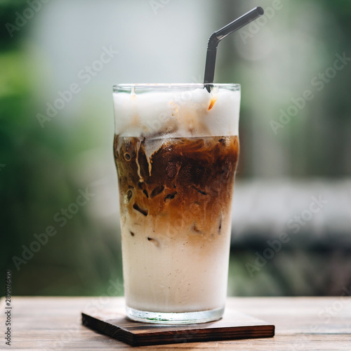 Close up shot of cold cappuccino in a glass with a straw on wooden table outdoors. Iced cappuccino is a tasty summertime drink that both cools you down and gives you an extra jolt of energy. photo