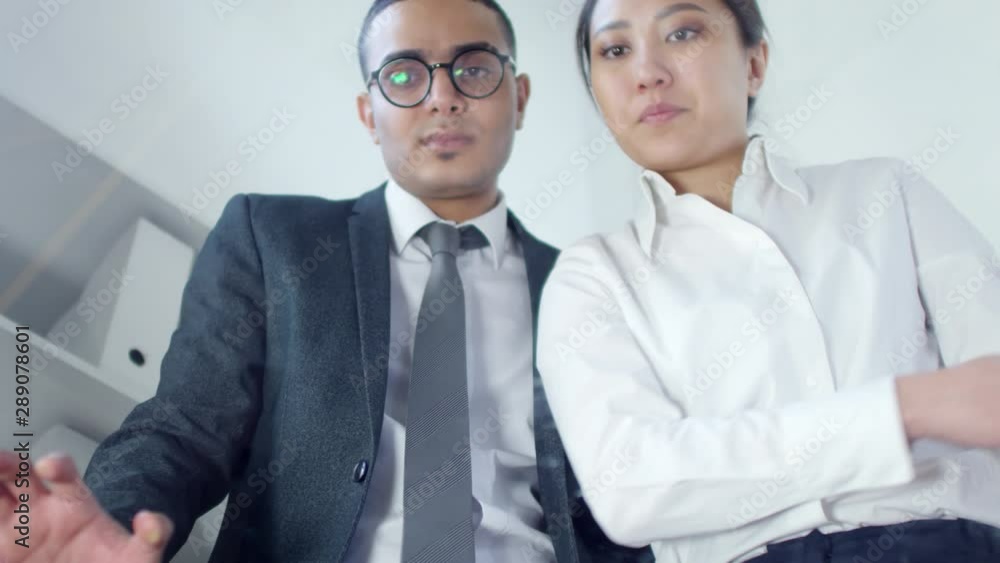 Low angle waistup shot of Asian female and Middle Eastern male colleagues in business attire