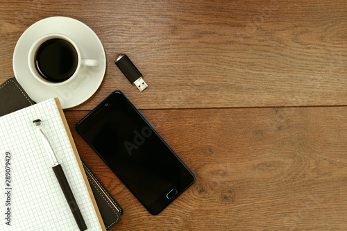 Office supplies on wooden table. Top view on composition of diary and smartphone near mug with americano on wooden table