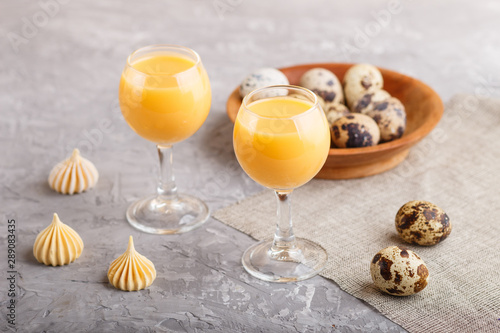 Sweet egg liqueur in glass with quail eggs and meringues on a gray concrete background. Side view