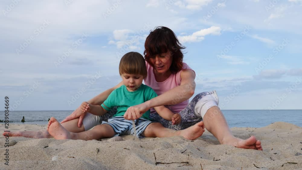 Mom playing with little child boy on seashore. Adult woman and her son enjoying summer day on beach. Family vacation at sea. Slow motion Mom playing with little child boy on seashore. Adult woman and her son enjoying summer day on beach. Family vacation at sea. Slow motion