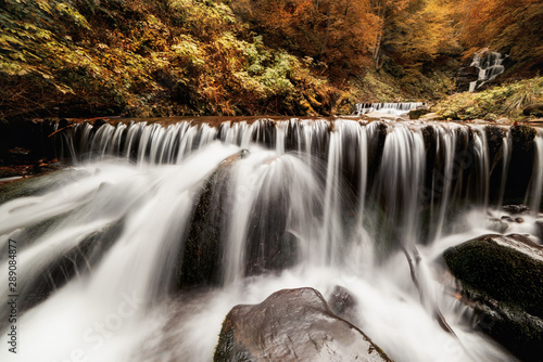 Cascade waterfall among the stones in the autumn forest. 