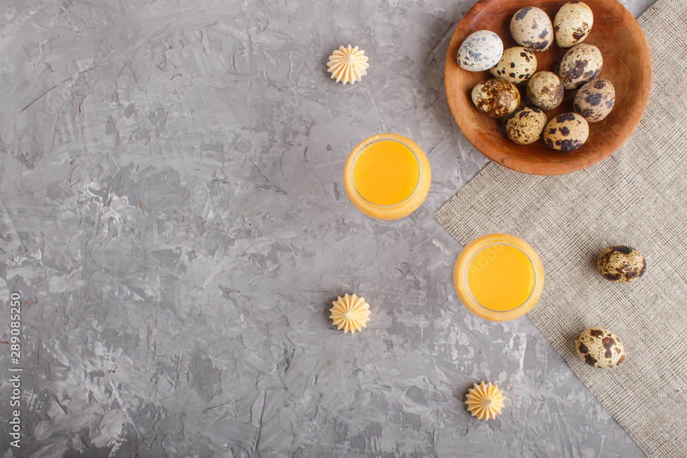 Sweet egg liqueur in glass with quail eggs and meringues on a gray concrete background. Top view, copy space. Sweet egg liqueur in glass with quail eggs and meringues on a gray concrete background. Top view, copy space.
