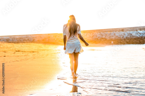 Lifestyle, a young brunette walking on the beach on a sunset
