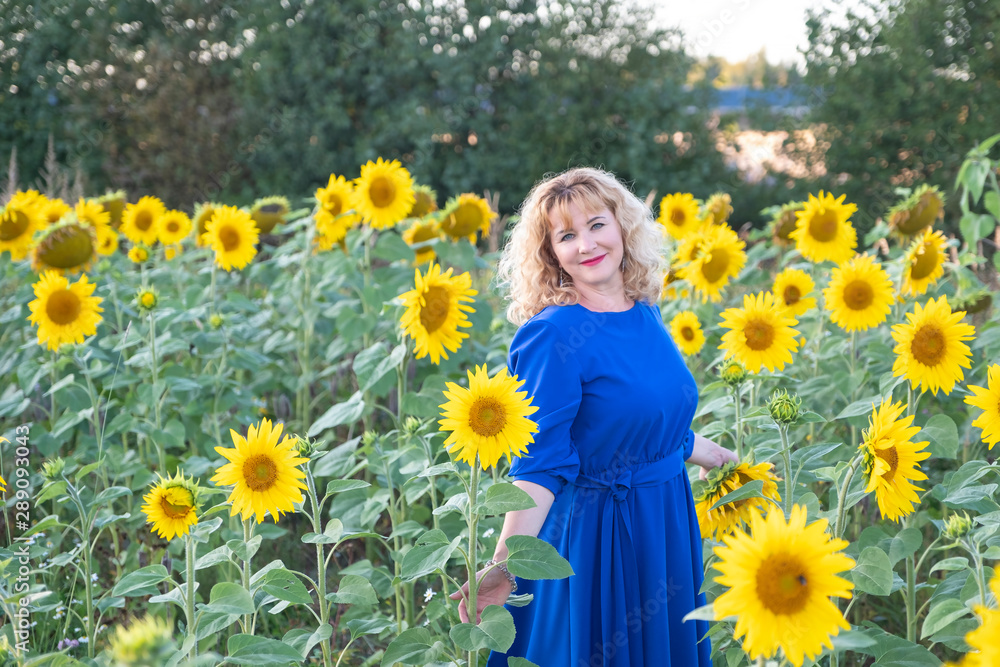 A woman in a blue dress and red hair is standing on a field with sunflower flowers at sunset. Copy space A woman in a blue dress and red hair is standing on a field with sunflower flowers at sunset. Copy space