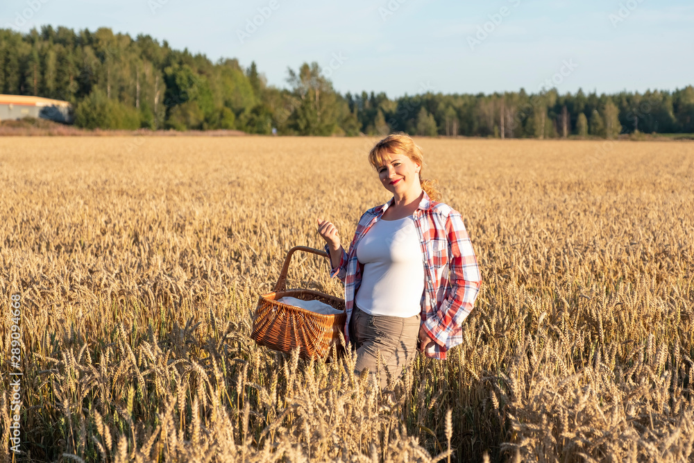 A girl with red hair and a wicker basket in her hands is standing on a field with ripe ears of corn. Countryside and sunset. A girl with red hair and a wicker basket in her hands is standing on a field with ripe ears of corn. Countryside and sunset.