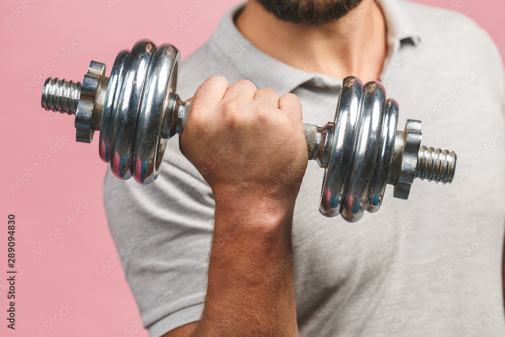 Close-up photo of man grabs a heavy dumbbell isolated over pink background with his hand. Concept lifting, fitness. Close-up photo of man grabs a heavy dumbbell isolated over pink background with his hand. Concept lifting, fitness.
