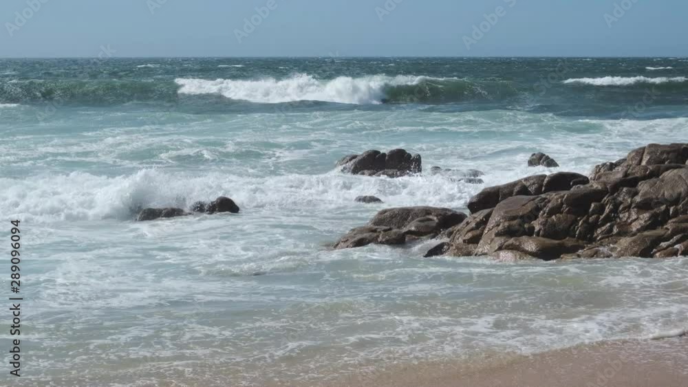 Waves splashing against rocks on beach, on a bright sunny day in summer with blue sky. Waves splashing against rocks on beach, on a bright sunny day in summer with blue sky.