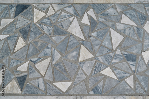The surface is lined with mosaic tiles of triangular shape and a variety of sizes. The triangles are arranged in a chaotic order. Between the tile joints in concrete. Background, texture, backdrop.