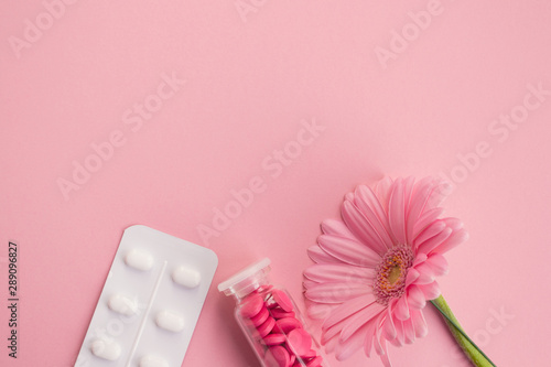 Women's health, medicine and healthcare concept. Pink tablets in a glass bottle, blister and flower on a light background. Copy space photo