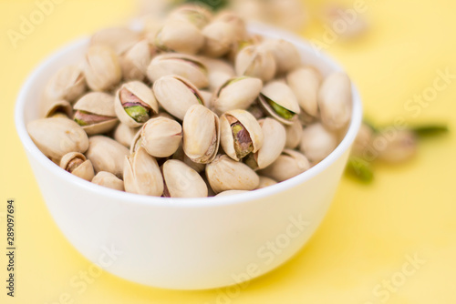Salted pistachios in a bowl on a yellow background