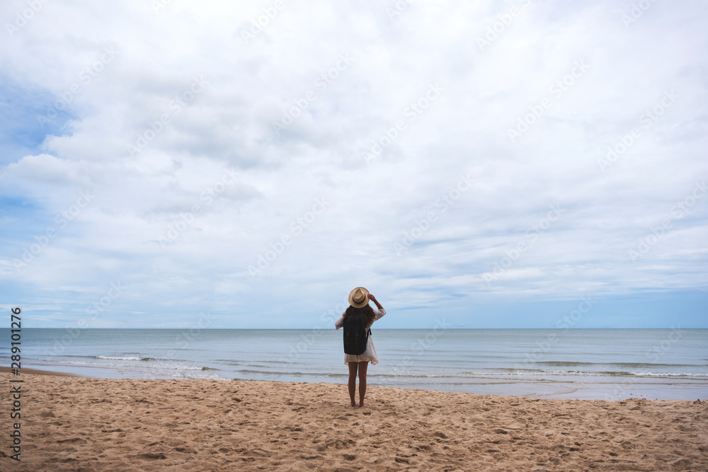 A female traveler with hat and backpack standing alone on the beach by the sea A female traveler with hat and backpack standing alone on the beach by the sea