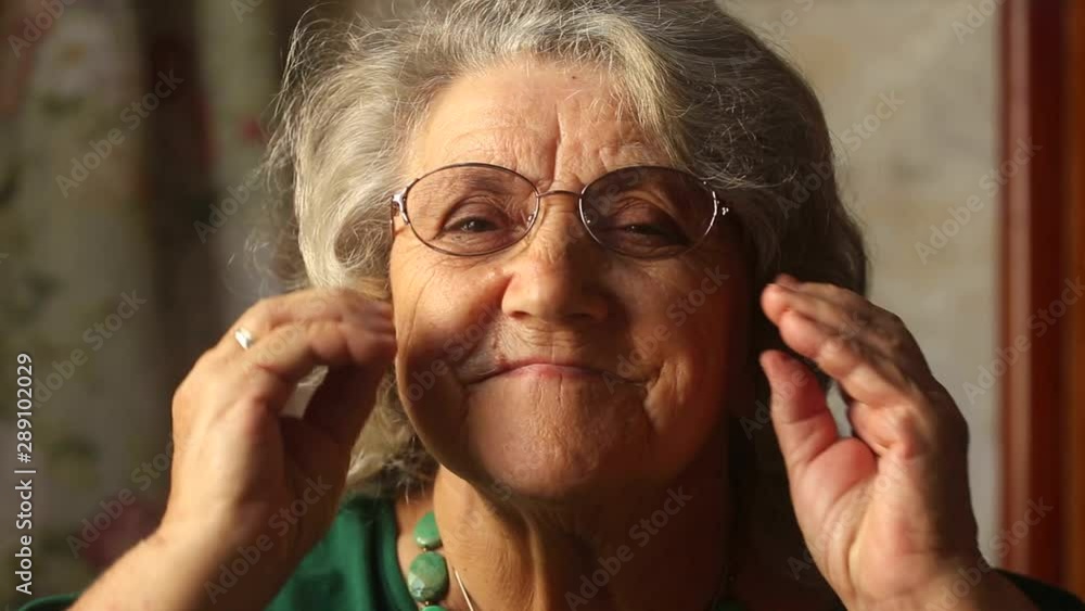 Elderly woman puts on glasses and looking away Elderly woman puts on glasses and looking away
