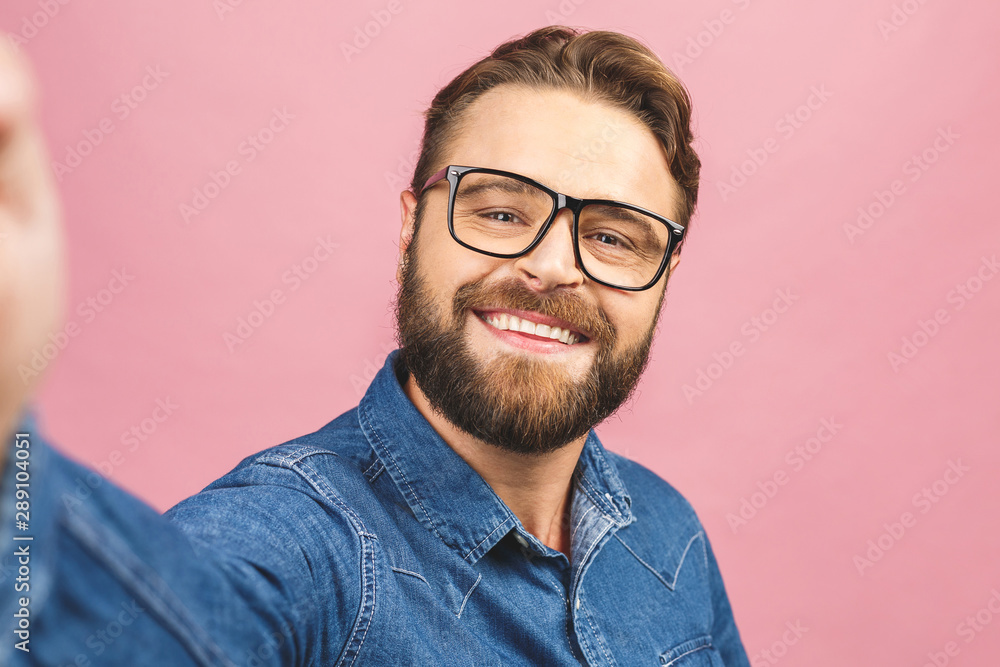 I love selfie! Handsome young man in shirt holding camera and making selfie and smiling while standing against pink background. I love selfie! Handsome young man in shirt holding camera and making selfie and smiling while standing against pink background.