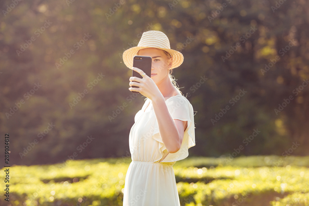 Beautiful serious young girl travel blogger takes photos and videos via smartphone in exotic country setting with clean air on sunny summer day. Concept of travel to environmentally friendly places