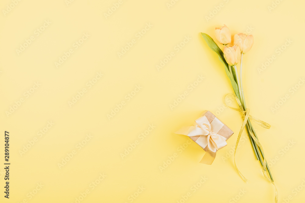 Fototapeta premium Yellow tulips flowers and gift box on pastel background. Festive birthday flat lay. Greeting for Womens or Mothers Day.