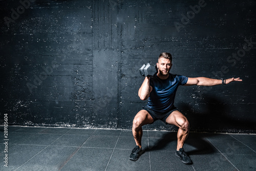 Fototapeta Naklejka Na Ścianę i Meble -  Young strong fit muscular sweaty man with big muscles strength cross workout training with dumbbells weights in the gym dark image with shadows real people