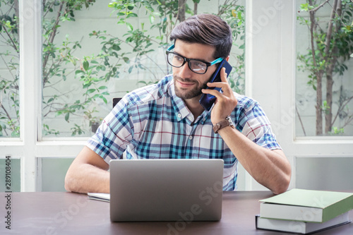Young caucasian businessman working at home office with laptop and talking on mobile phone.