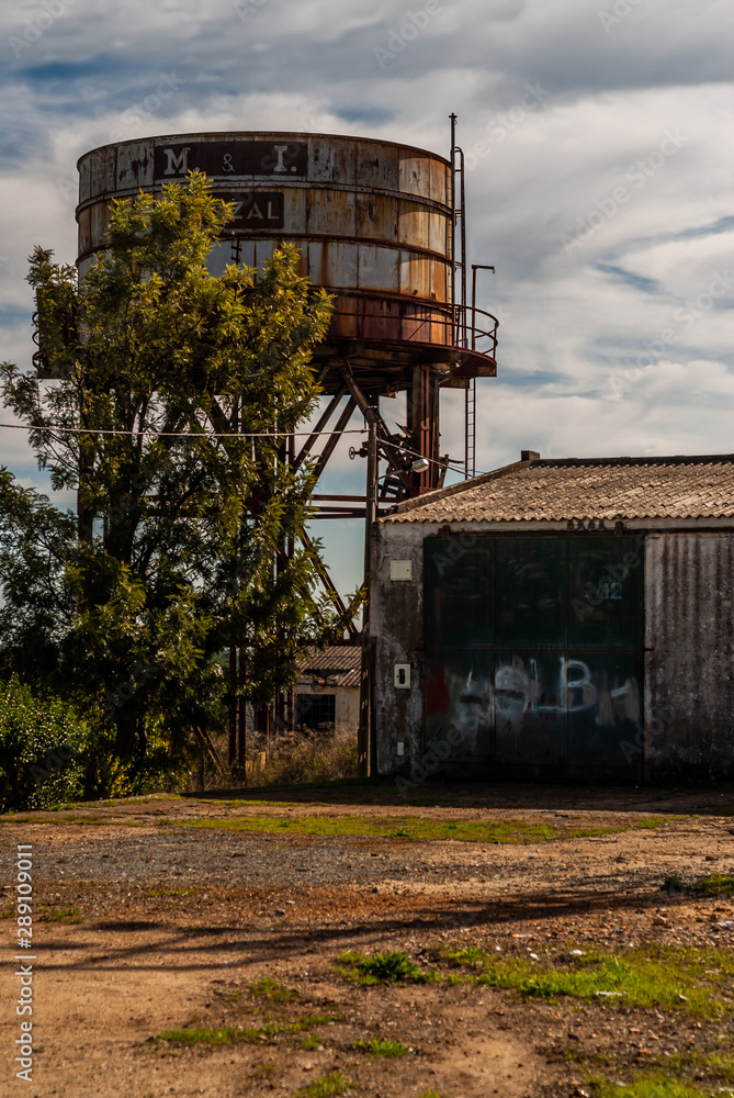 Louzal or Lousal pyrite Mine in Portugal, view of the rusty vintage water tank and a closed warehouse in the abandoned railway station. Louzal or Lousal pyrite Mine in Portugal, view of the rusty vintage water tank and a closed warehouse in the abandoned railway station.