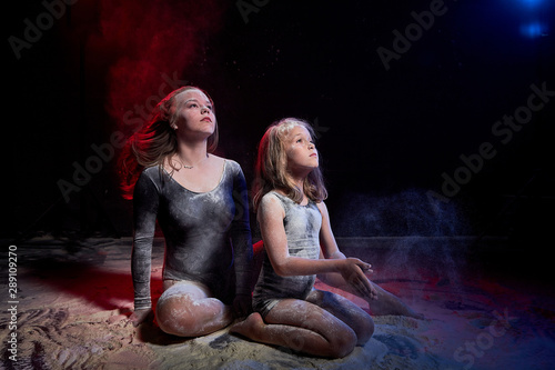 Two sisters in black studo with red and blue light during photoshoot with flour