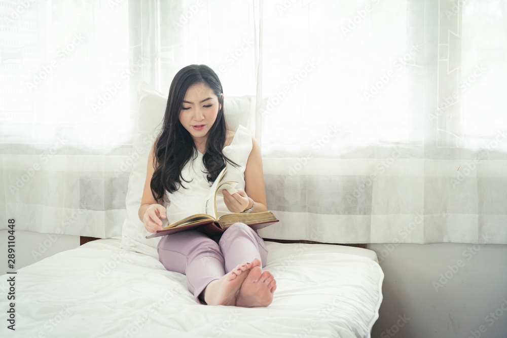 Beautiful asian girl reading book in the morning on her bed.