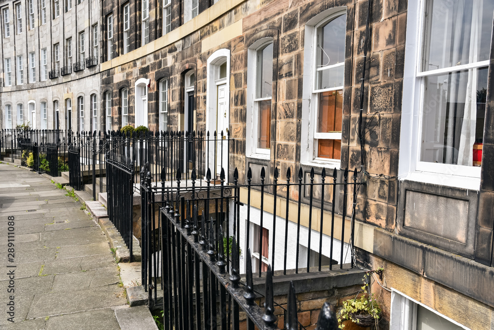 Extrerior of traditional Scottish stone town houses with metal fences along a pavement. Edinburgh, Scotland, UK.