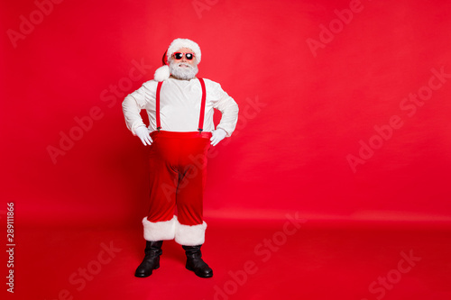 Full body photo of positive funny fat overweight santa claus with style eyeglasses big belly ready to celebrate newyear party standing isolated over red background wearing trousers pants