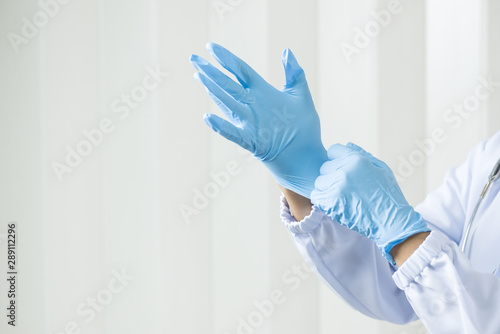 Woman doctor putting blue latex medical gloves on white wall background.Surgeon wearing gloves before surgery at operating room.Risk management protection health care concept. photo