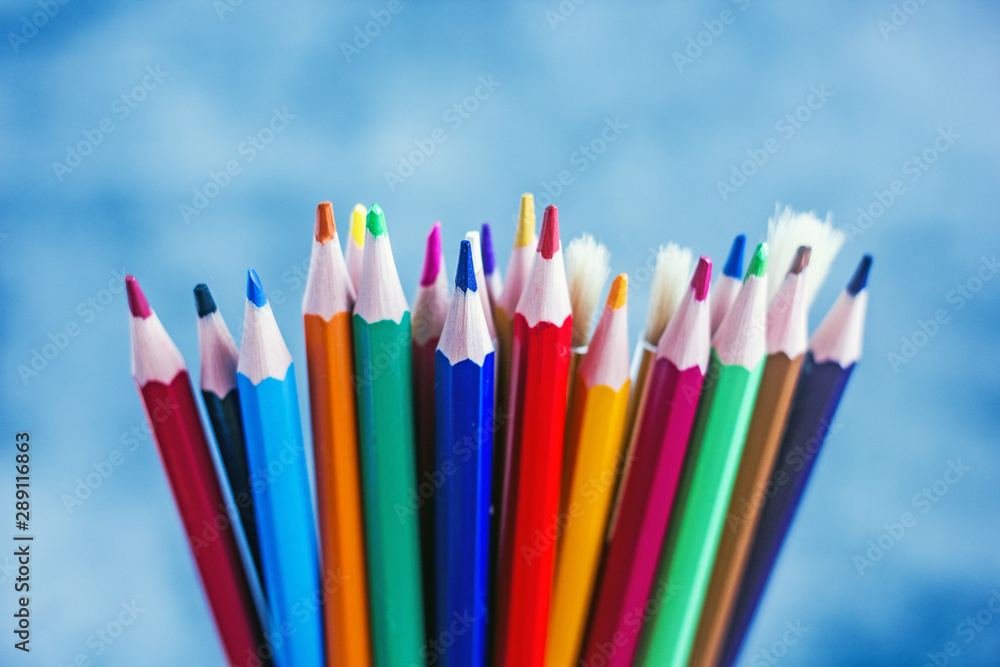 Bunch of colorful art supplies Closeup set of bright multicolored pencils and brushes placed against blue background Bunch of colorful art supplies Closeup set of bright multicolored pencils and brushes placed against blue background