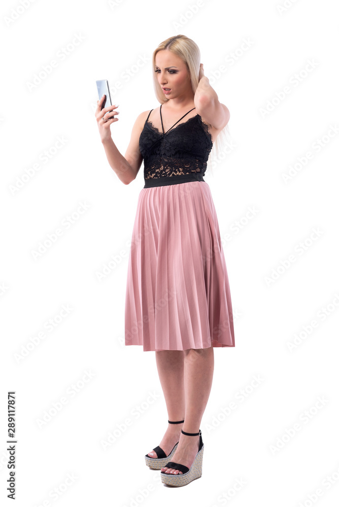 Young shocked woman looking at phone screen with angry expression. Full body isolated on white background. Young shocked woman looking at phone screen with angry expression. Full body isolated on white background.