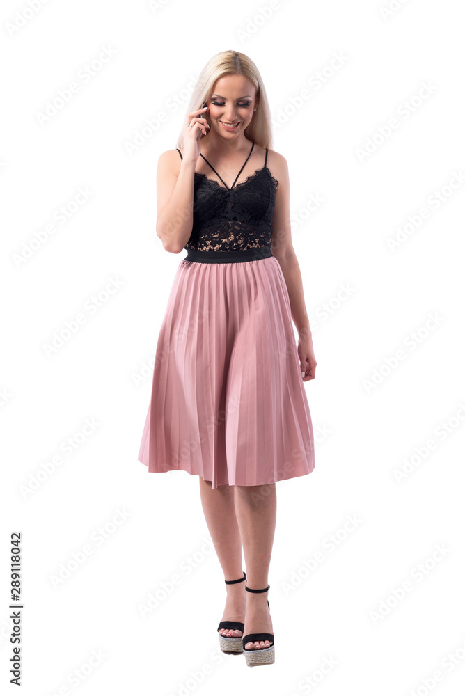 Happy relaxed young blonde stylish woman walking and speaking on the mobile phone looking down. Full body isolated on white background. Happy relaxed young blonde stylish woman walking and speaking on the mobile phone looking down. Full body isolated on white background.