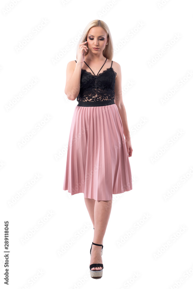Serious busy elegant young woman walking and talking on the phone looking down. Full body isolated on white background. Serious busy elegant young woman walking and talking on the phone looking down. Full body isolated on white background.