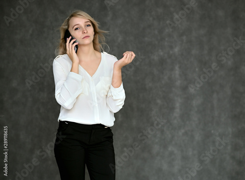 Portrait of a pretty blonde girl in a white blouse on a gray background. Right in front of the camera in various poses.