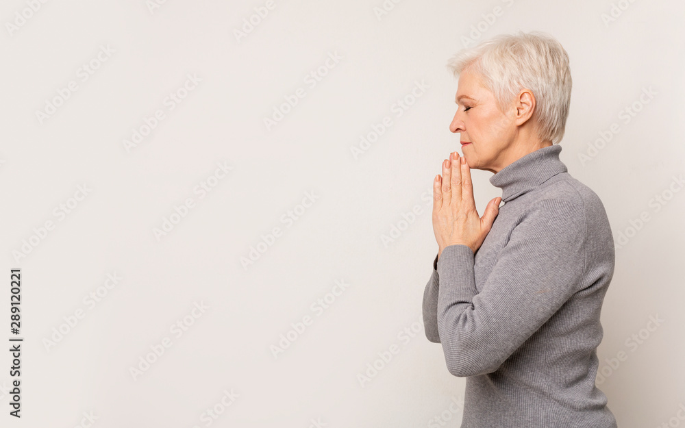Beautiful mature woman praying with hands clasped near face Beautiful mature woman praying with hands clasped near face