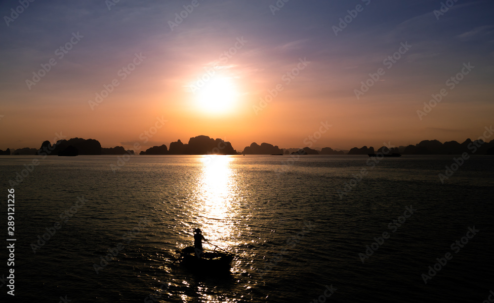 Sunset at the limestone rock formations of Halong Bay and Bai Tu Long Bay, Vietnam. Silhouette of a rowing boat.