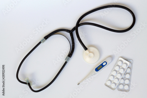 medical stethoscope with pills and thermometer on white background top view