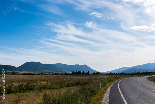 Empty asphalt road, vulcanic mountains against beautiful blue sky with white clouds near Tusnad Bai in Transylvania, Romania.