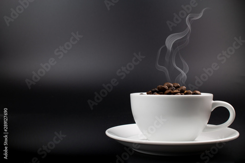cup of coffee and coffee beans on dark background with smoke