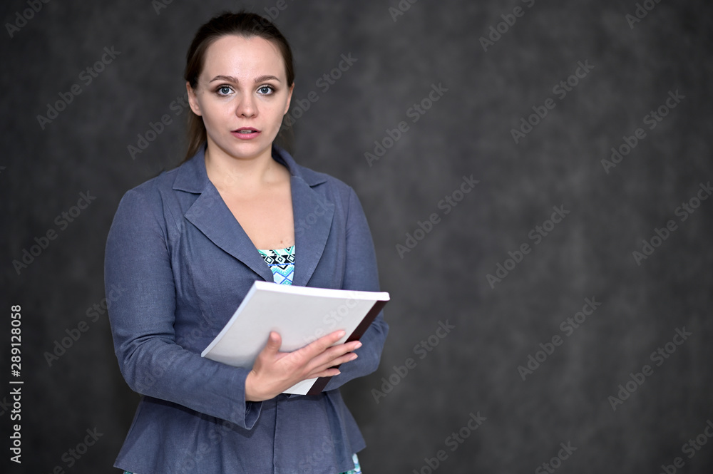 Portrait of a pretty manager woman on a dark background in a gray business suit with a folder in her hands. Standing right in front of the camera in various poses. Portrait of a pretty manager woman on a dark background in a gray business suit with a folder in her hands. Standing right in front of the camera in various poses.