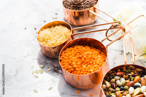 Copper measuring cups on marble table with beans and cereals in the kitchen. Cooking or bulk food purchase concept photo