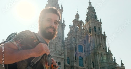 Portrait of happy male pilgrim looking at camera in Santiago de Compostela, Spanish town at the end of Camino de Santiago or Way of St James. Young man smiling in Spain, slow motion photo