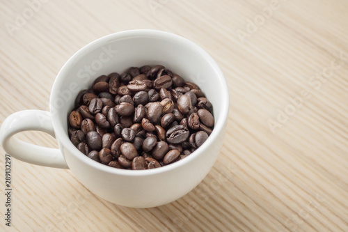 fresh roasted coffee beans in white cup on wood table