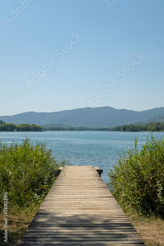 Wooden path on the shore of a blue lake in Banyoles Catalonia under a sunny blue sky on a summer landscape © jordieasy