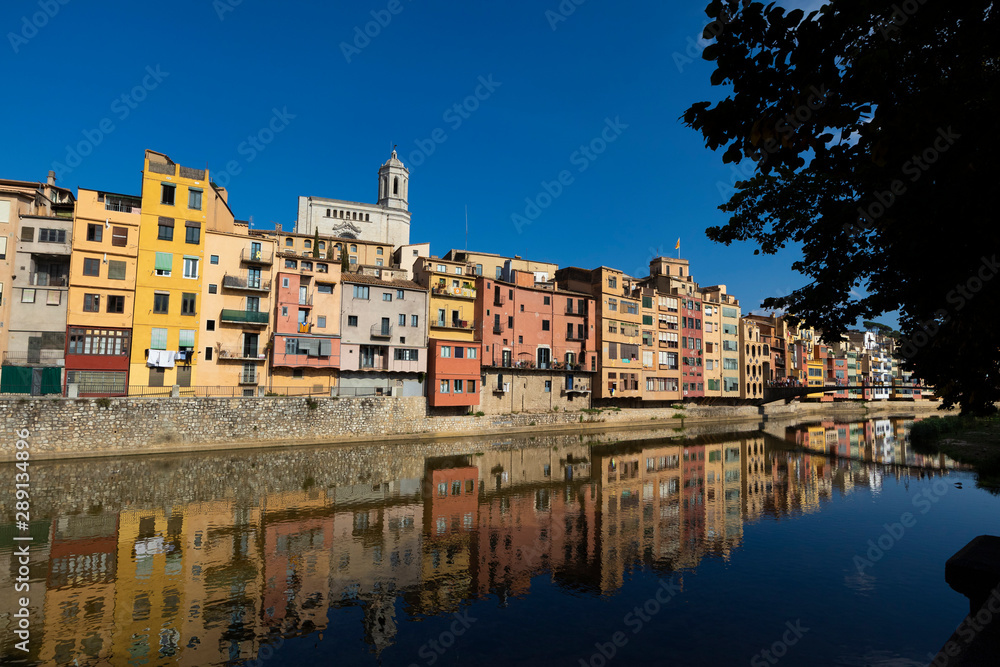 Girona city skyline with river houses colourful facades reflected on quiet river water on a blue summer sunny sky
