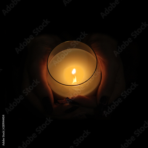 Burning candle in the hands in complete darkness.